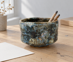 Ambientazione creata con IA : Chawan blu grigio con zone scure, su una scrivania con piccoli oggetti.