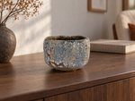 AI-generated setting : Pale blue chawan with an ochre mosaic, on a walnut console.