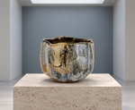 AI-generated setting : Blue grey chawan with ochre runs, on a travertine plinth.