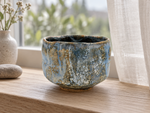 Ambientazione creata con IA : Chawan azzurro tenue con colature ocra, vicino a una finestra.