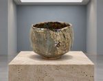 AI-generated setting : Grey blue chawan with ochre patches, on a travertine plinth.