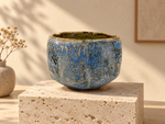Ambientazione creata con IA : Chawan blu con reticolo ocra, su un piedistallo.