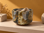 Ambientazione creata con IA : Chawan blu grigio con zone ocra, su una console con un nastro.