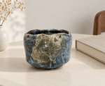 Ambientazione creata con IA : Chawan crema e blu con bordo ondulato, su un tavolo con libri.