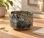 Ambientazione creata con IA : Chawan blu scuro con zone crema, su una scrivania con piccoli oggetti.