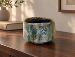 AI-generated setting : Grey green chawan with a blue interior, on a walnut console.
