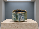 AI-generated setting : Grey green chawan with a blue interior, on a travertine plinth.