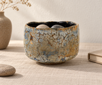 Ambientazione creata con IA : Chawan crema con trama ocra, su un tavolo con ciottoli.
